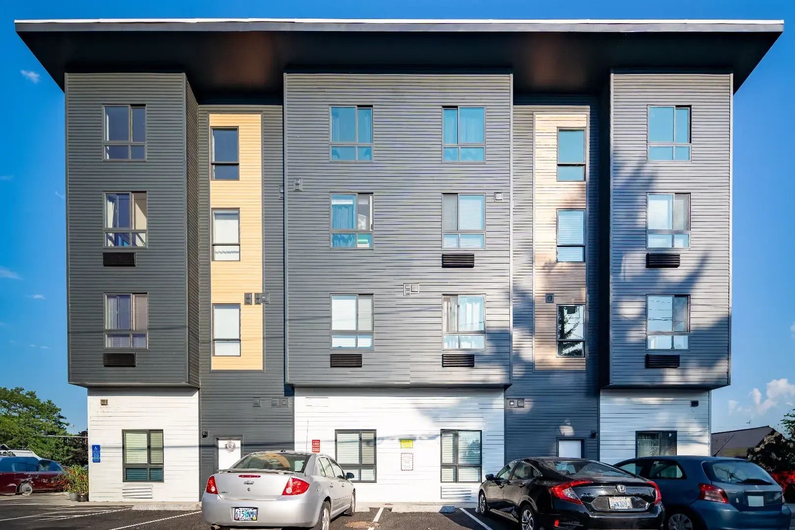 Modern apartment building with gray siding and parked cars in front
