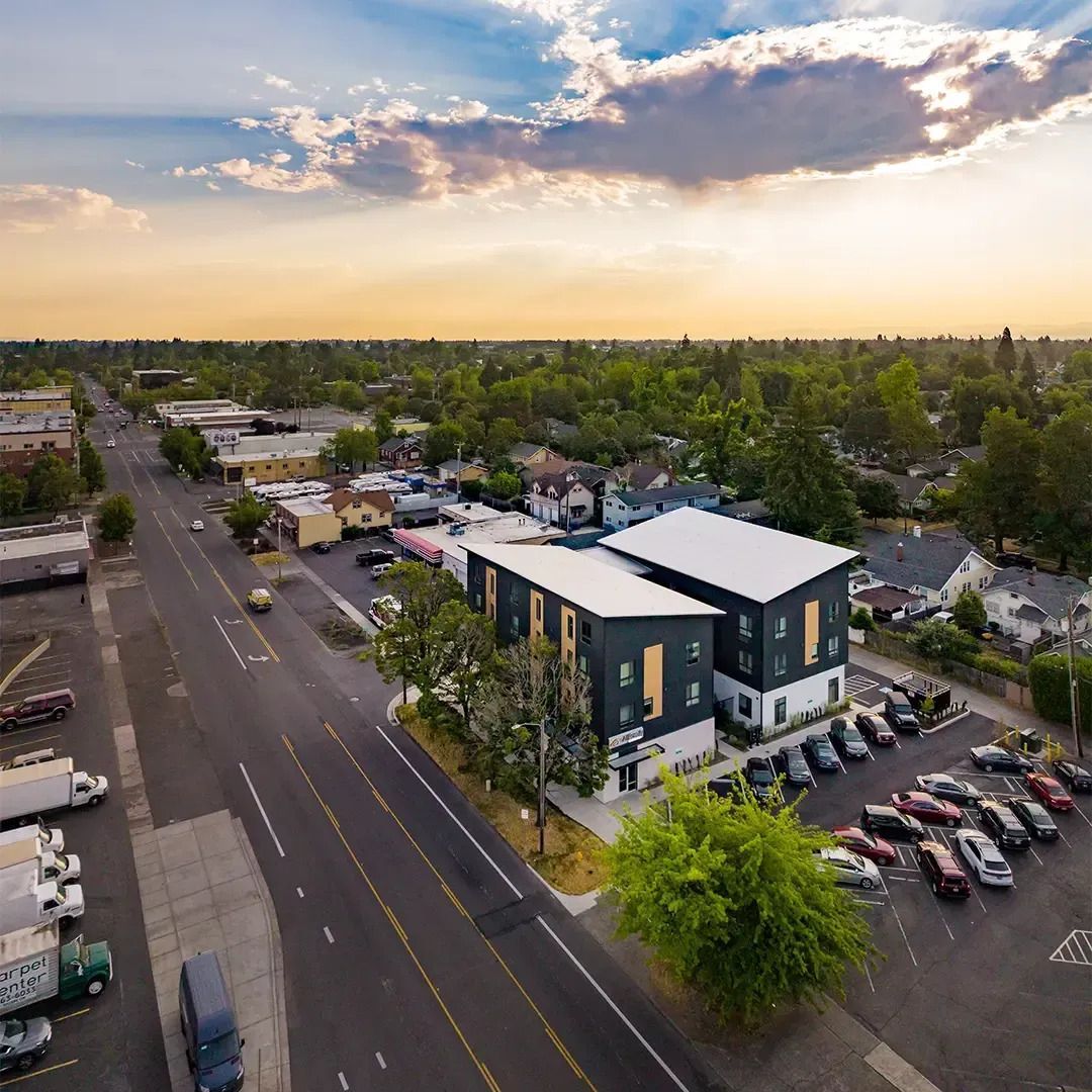 Aerial view of a modern office building beside a road and parking lot at sunset.