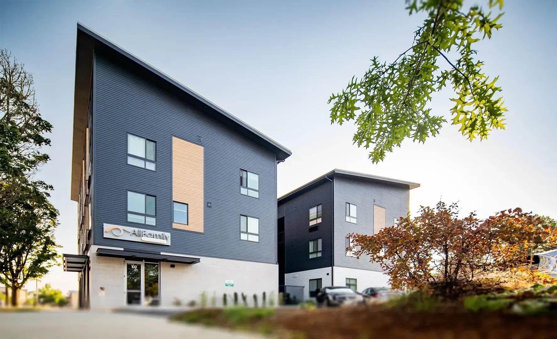 Modern blue-gray apartment buildings with large windows and trees on a sunny day