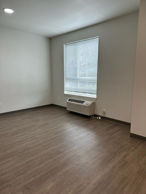 Empty room with gray walls, wood floor, and a window air conditioner beneath a window.