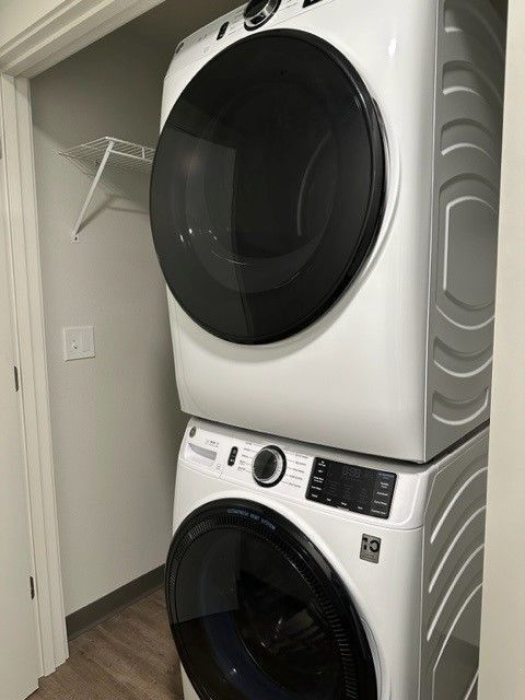 Stacked white washer and dryer in a laundry closet with an open door and shelving.