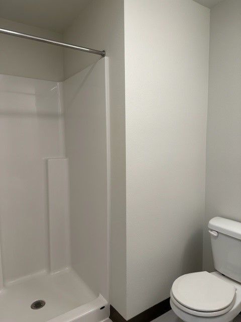 Small bathroom with shower stall, white walls, and a toilet beside it.