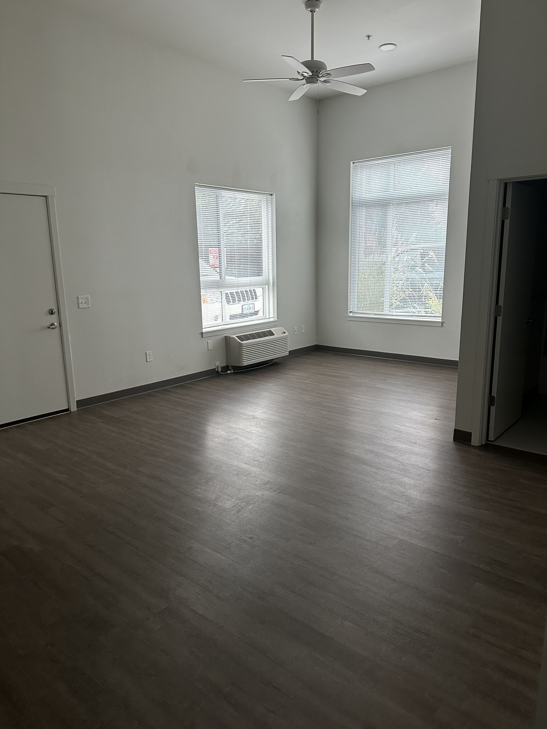 Empty room with dark wood floors, two windows, ceiling fan, and a radiator under one window.