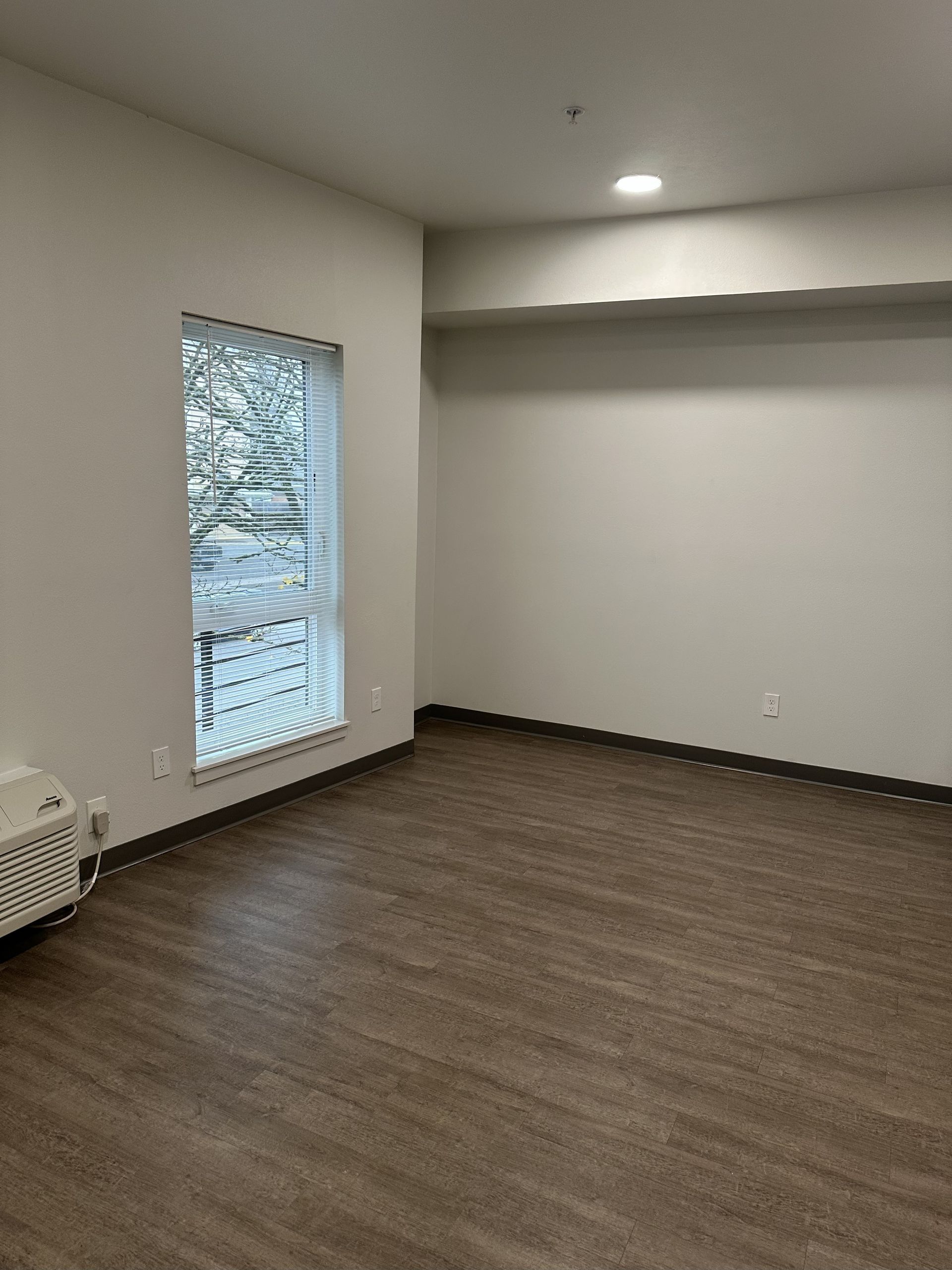 Empty carpeted room with white walls, recessed light, and a window with blinds