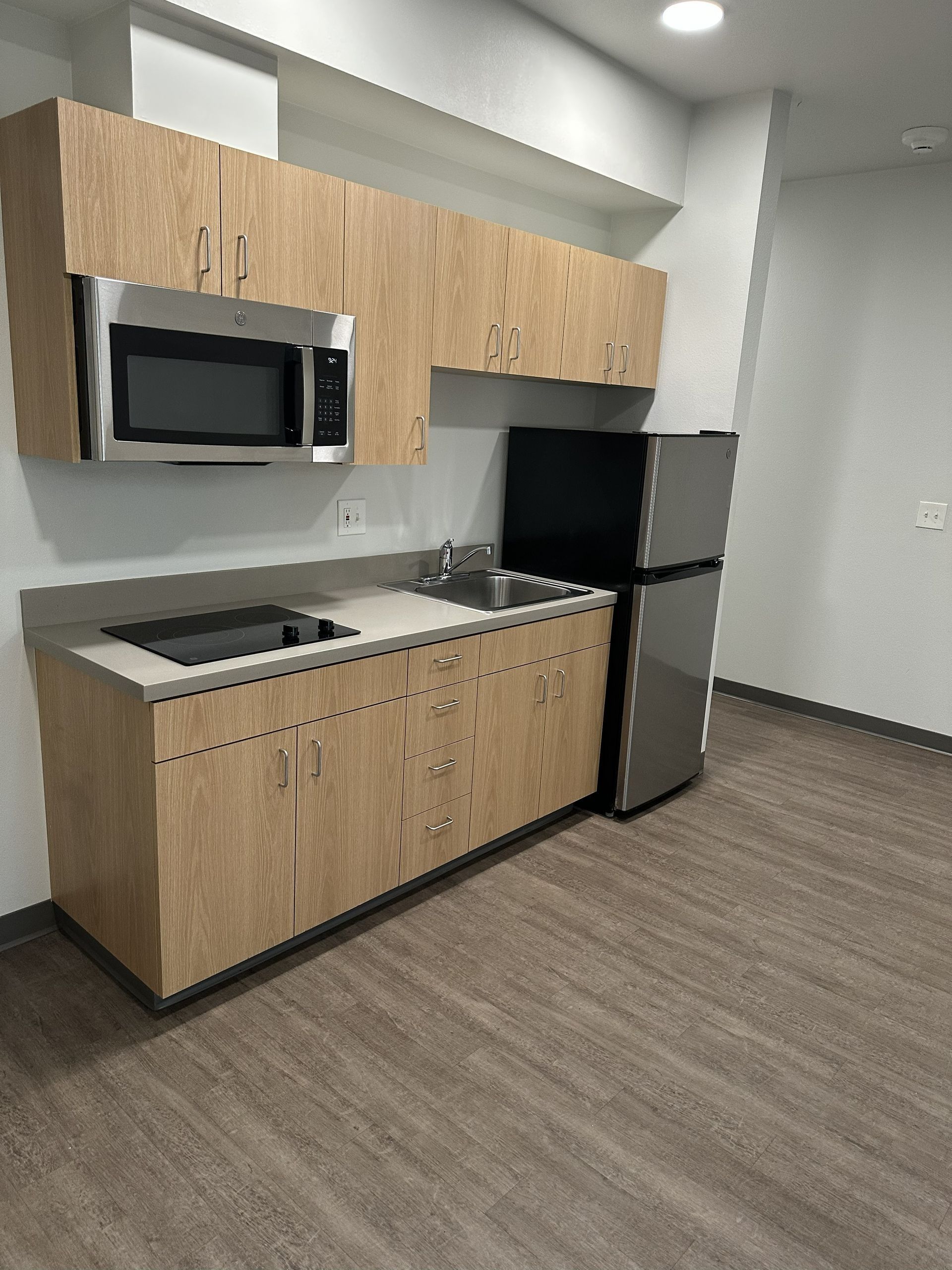 Compact apartment kitchenette with wood cabinets, stainless appliances, and gray flooring