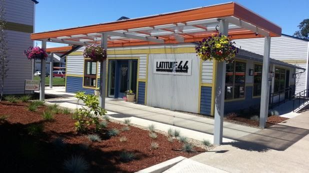Modern storefront with orange awning, hanging flowers, and blue-trimmed entrance in a shopping plaza