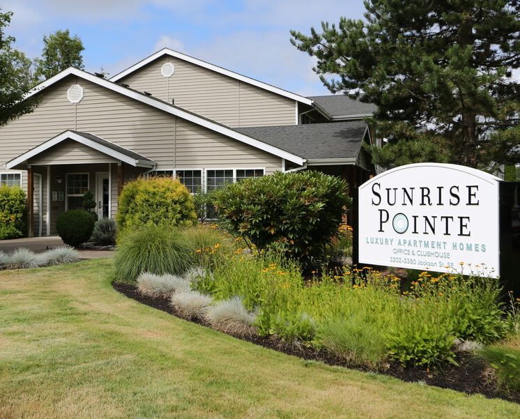 Suburban apartment building with gray siding, black shutters, and landscaped flower beds in front