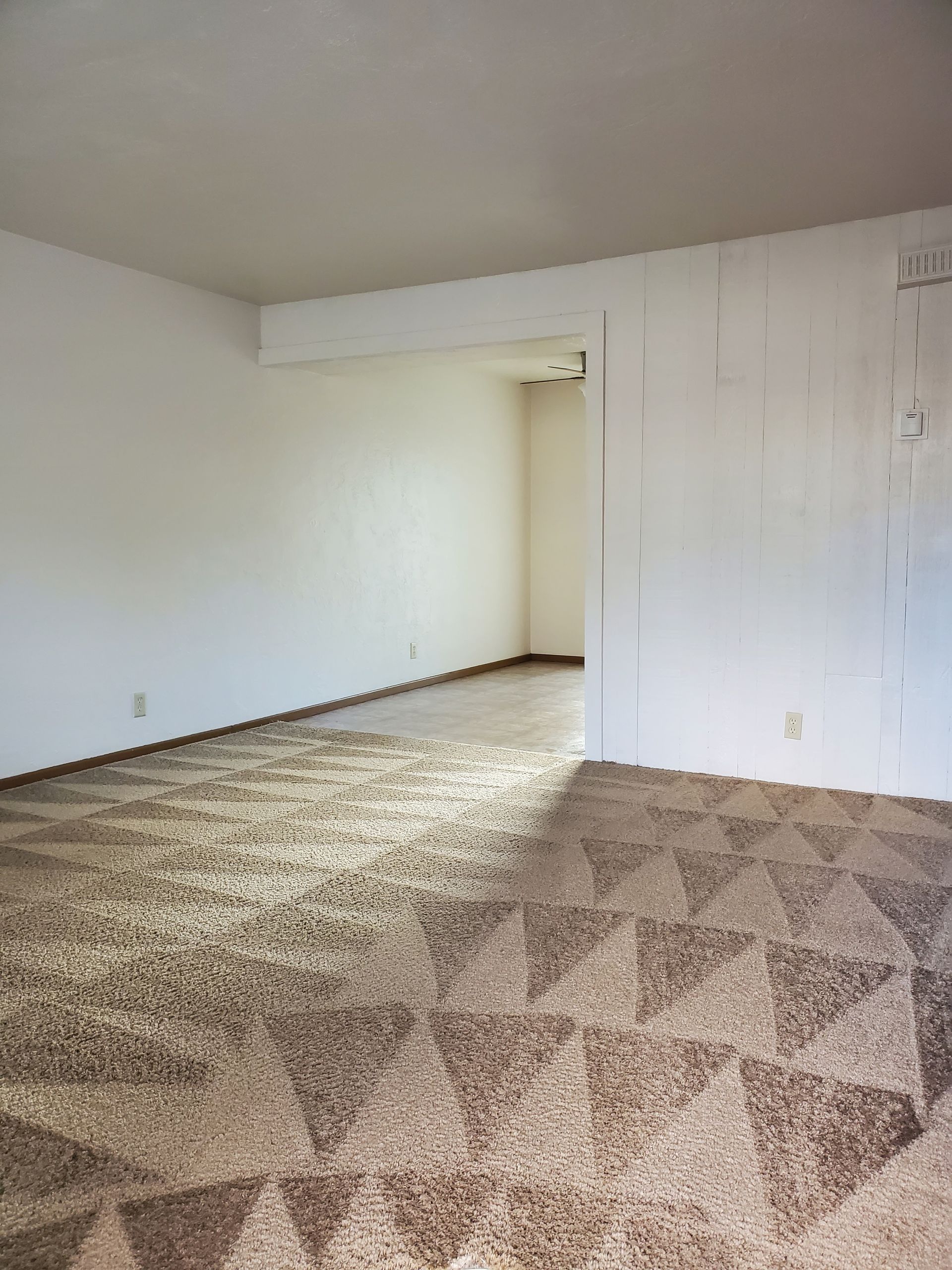 Empty carpeted room with white walls, a partial divider, and a doorway opening to a hall.