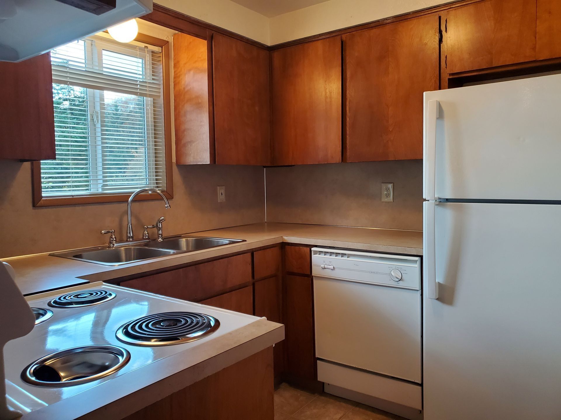 Cozy kitchen with wood cabinets, white appliances, sink by a window, and electric stove
