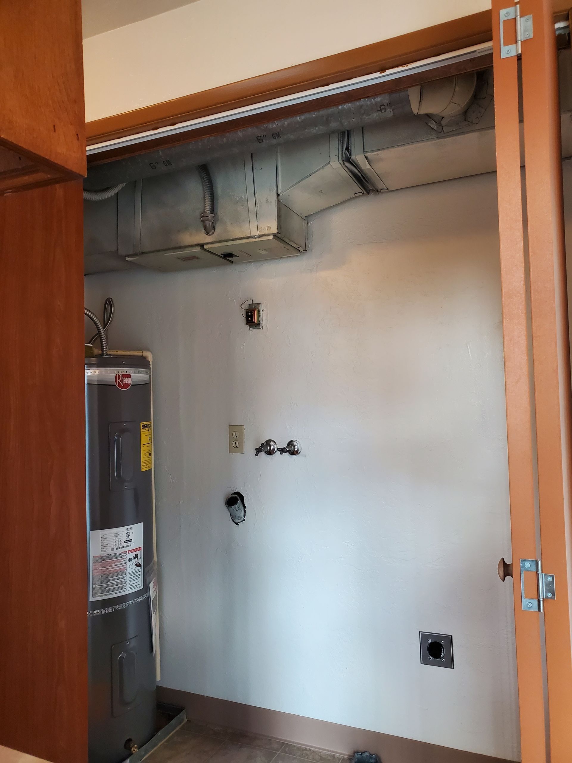 Empty closet with open wooden doors, white wall, exposed ductwork, and a water heater on the left.