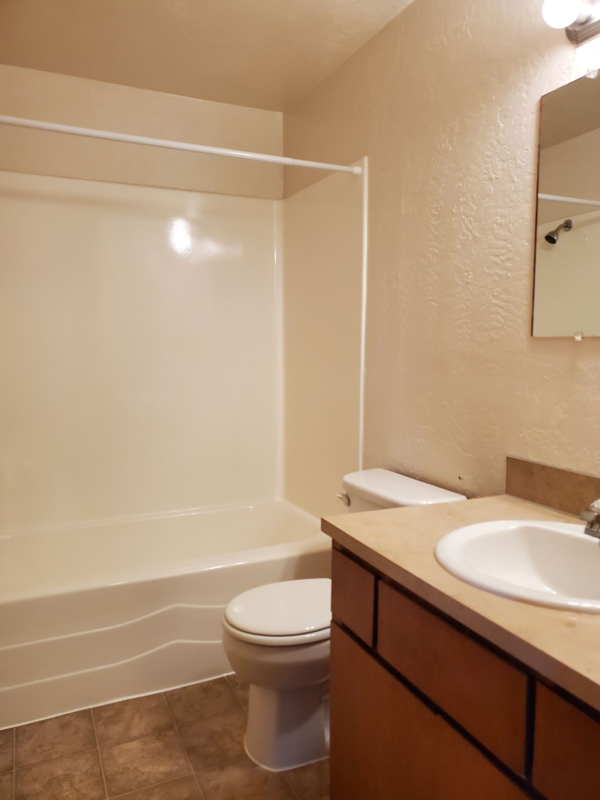 Bathroom with white tub-shower, toilet, and sink vanity in beige tones