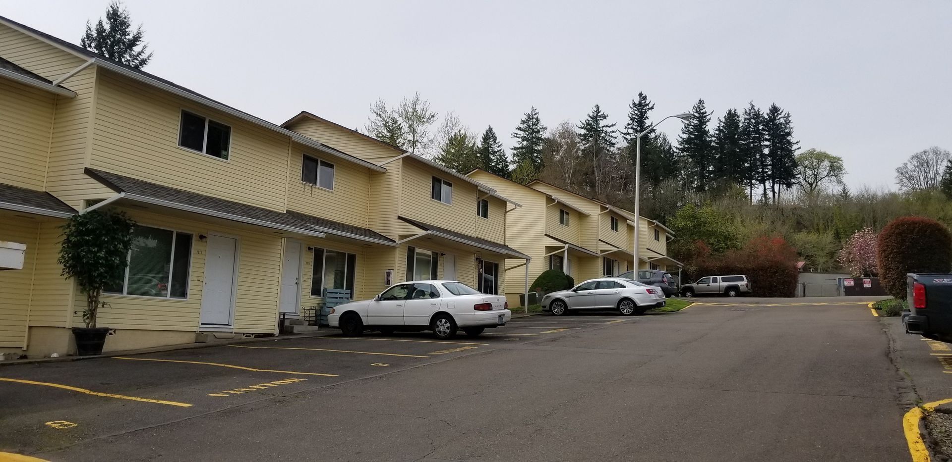 Long beige apartment building with parked cars along a driveway on an overcast day