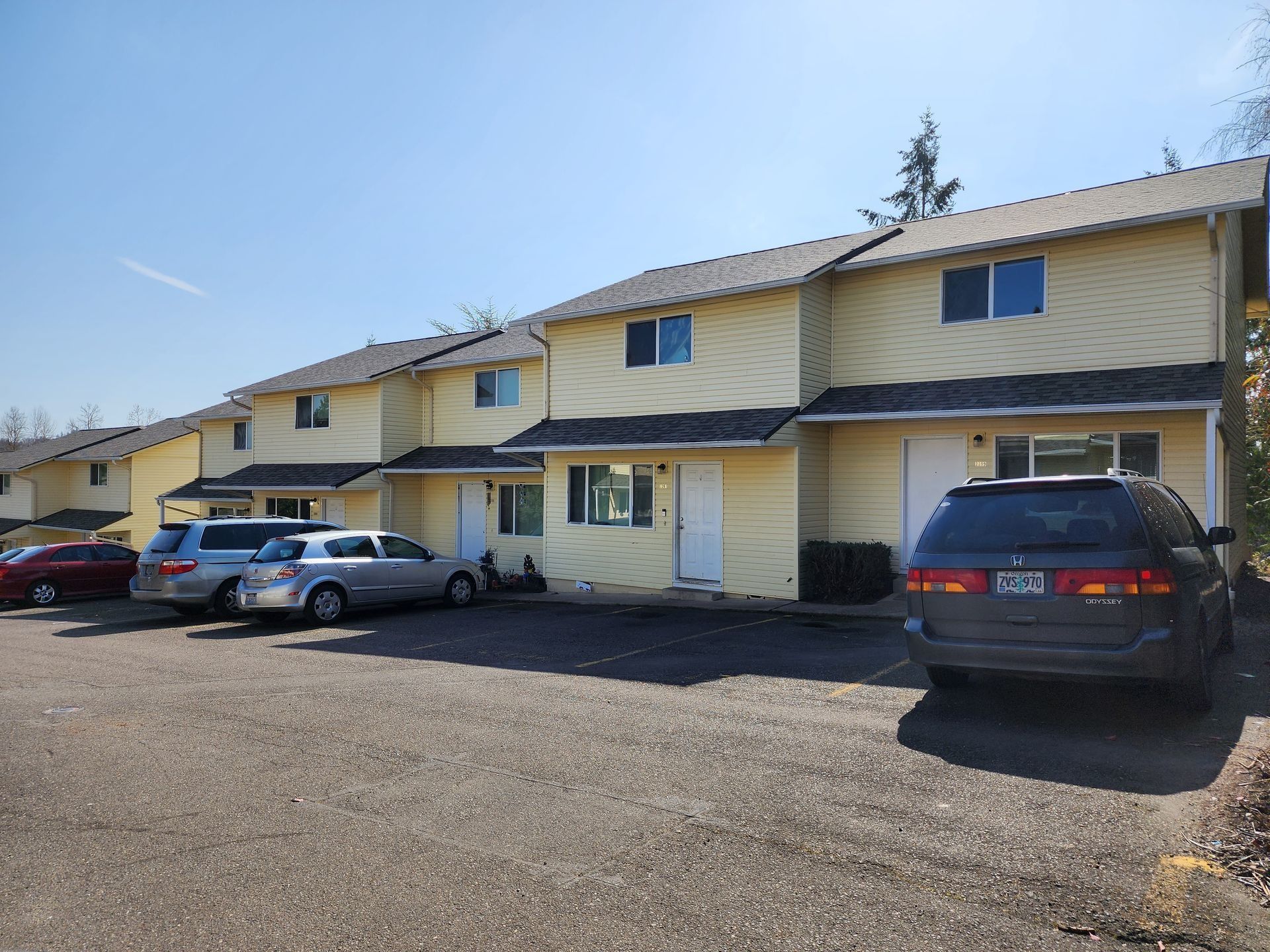 Row of yellow townhouses with parked cars on a gravel lot under a clear sky