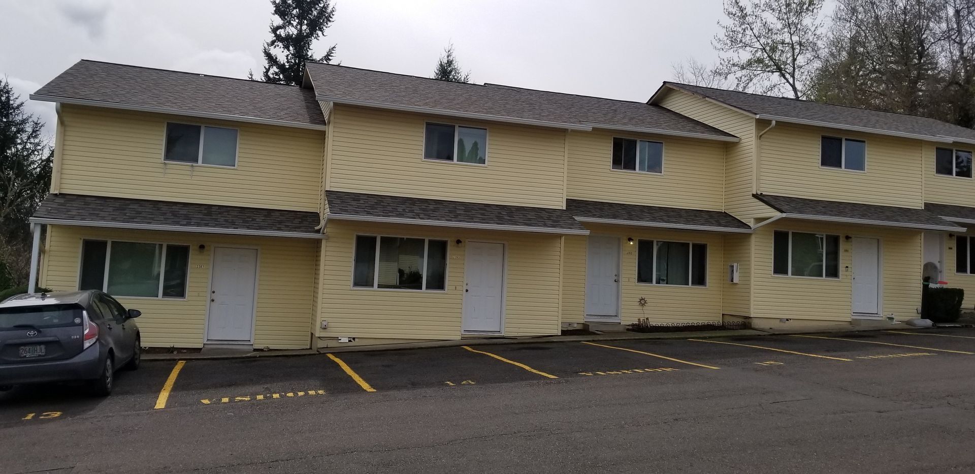 Yellow two-story apartment building with white trim and parked cars in front