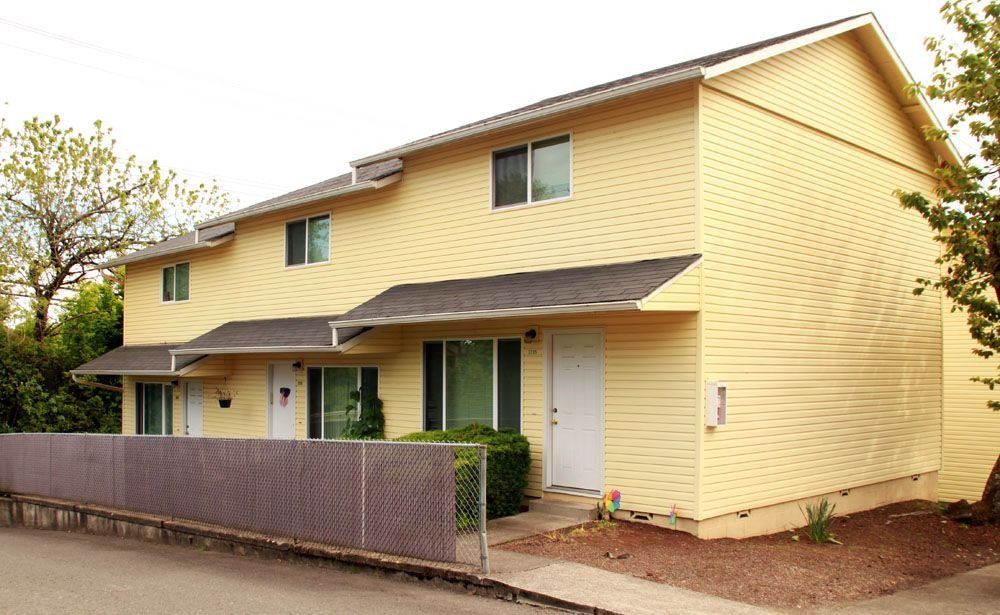 Yellow two-story apartment building with a covered entry and fenced front walkway