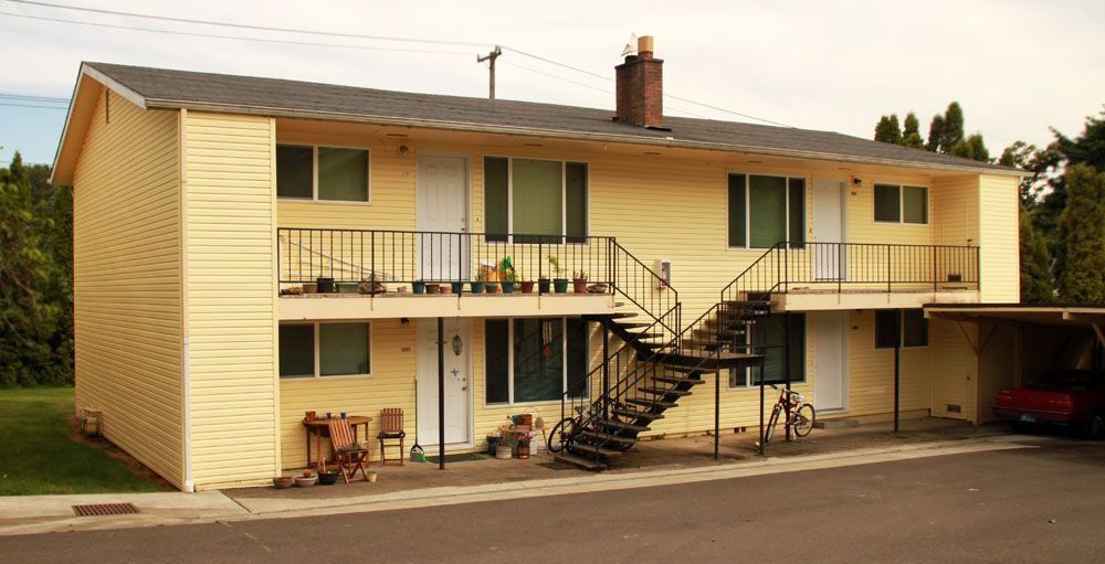 Two-story beige apartment building with exterior stairs and covered parking at sunset