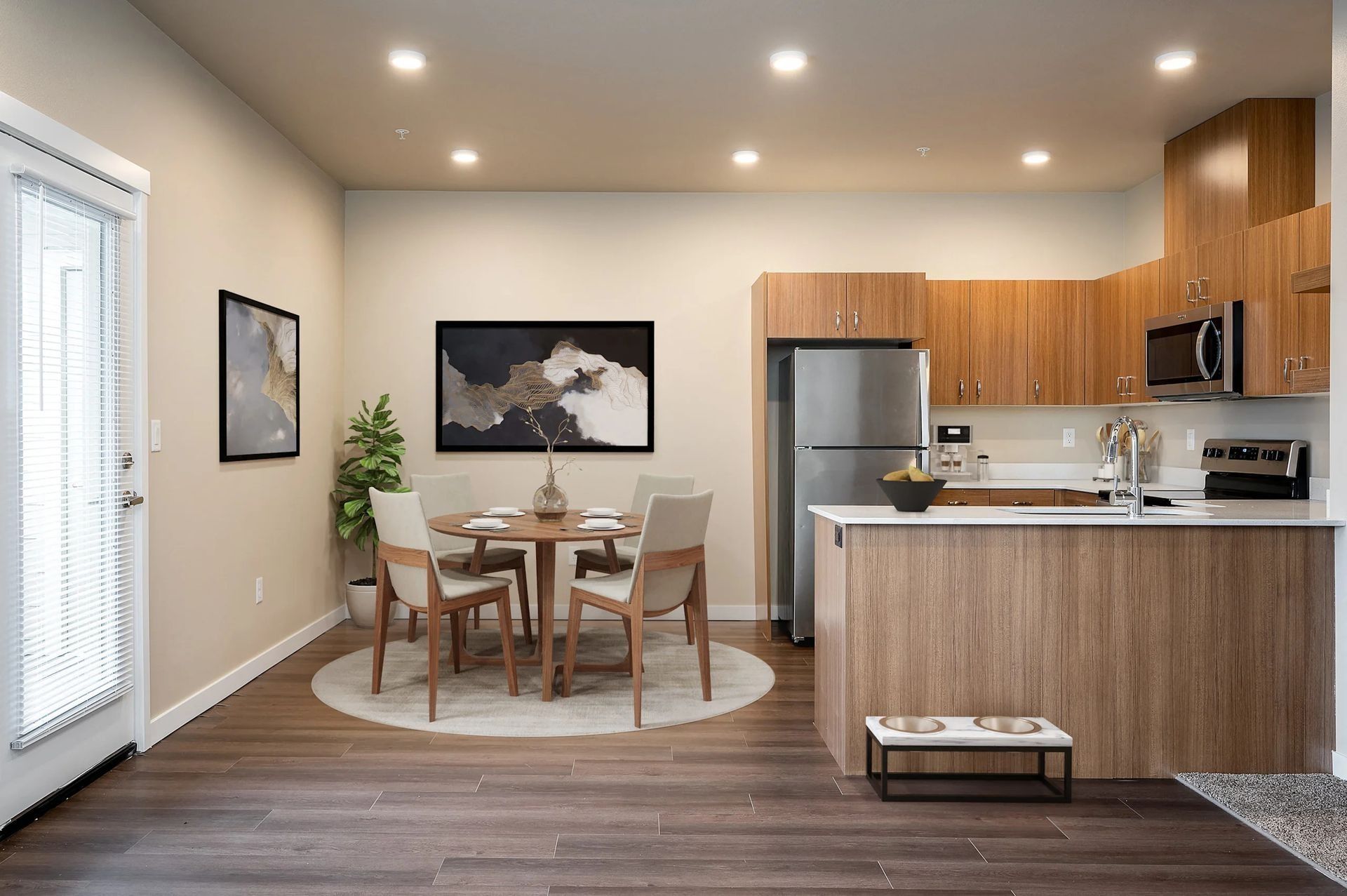 Modern kitchen and dining area with wood cabinets, stainless appliances, and a round table on a rug.