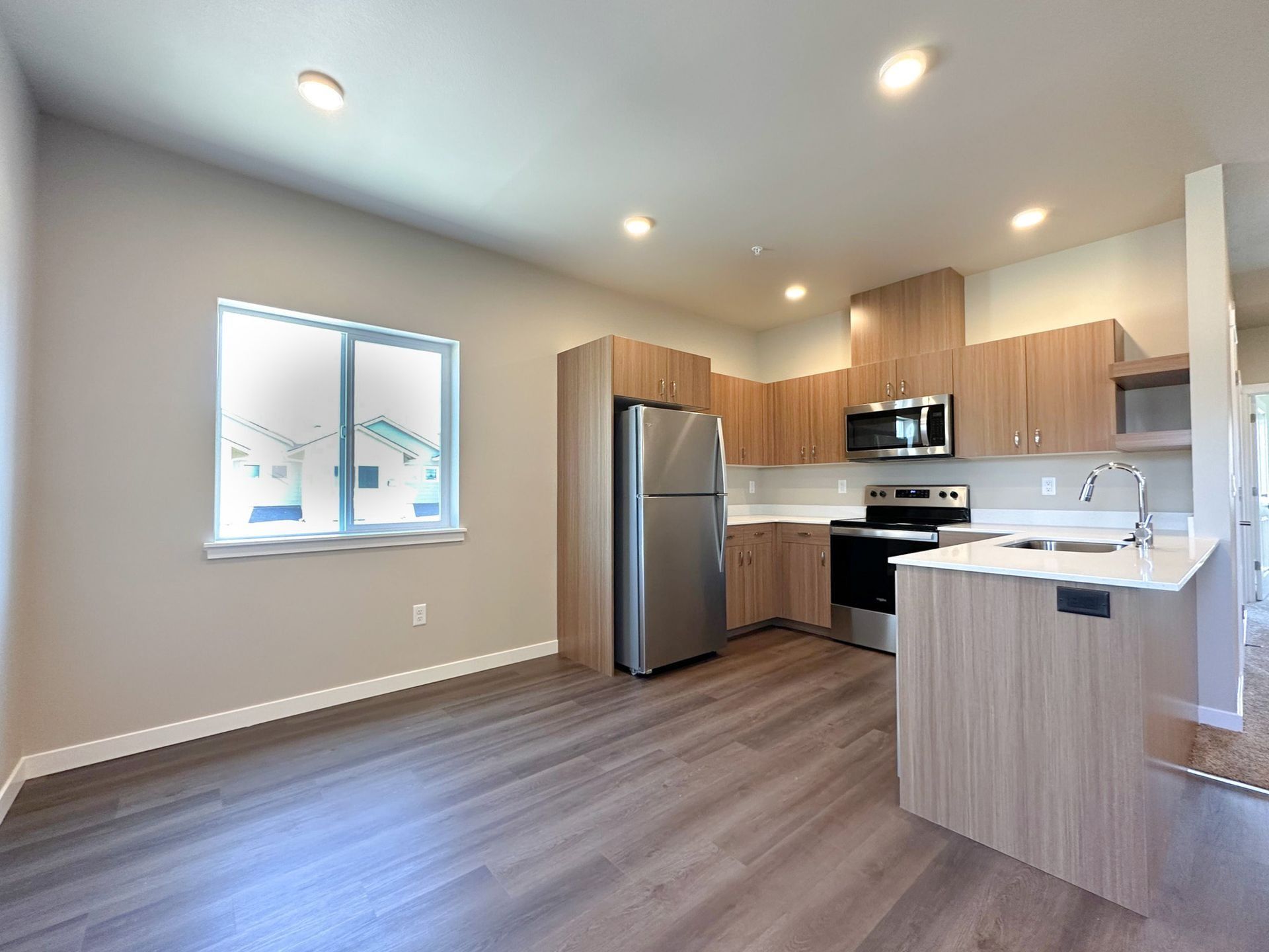 Empty modern kitchen with stainless steel fridge, wood cabinets, and gray flooring