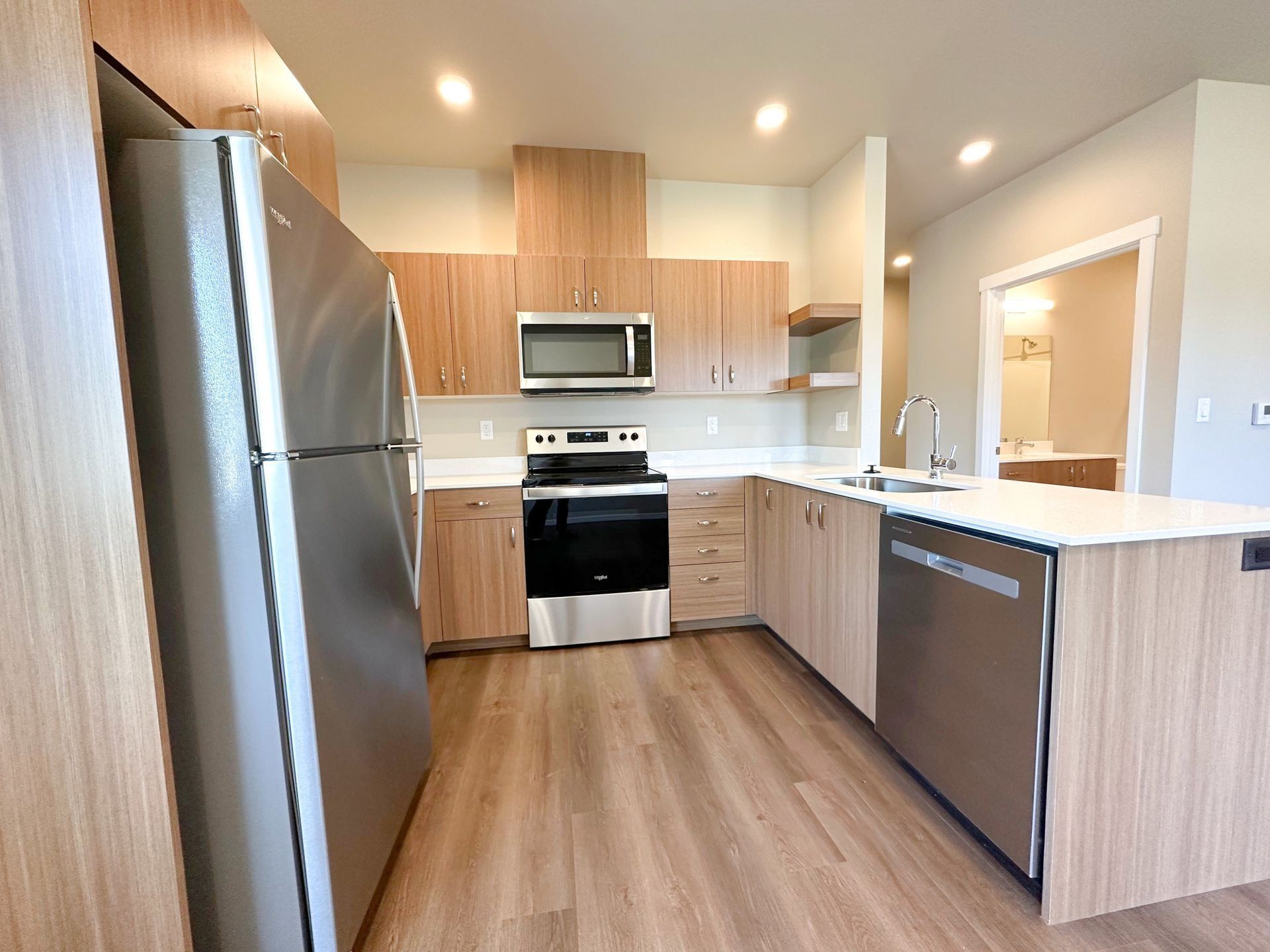 Modern kitchen with stainless steel appliances, wood cabinets, and a light-colored island.