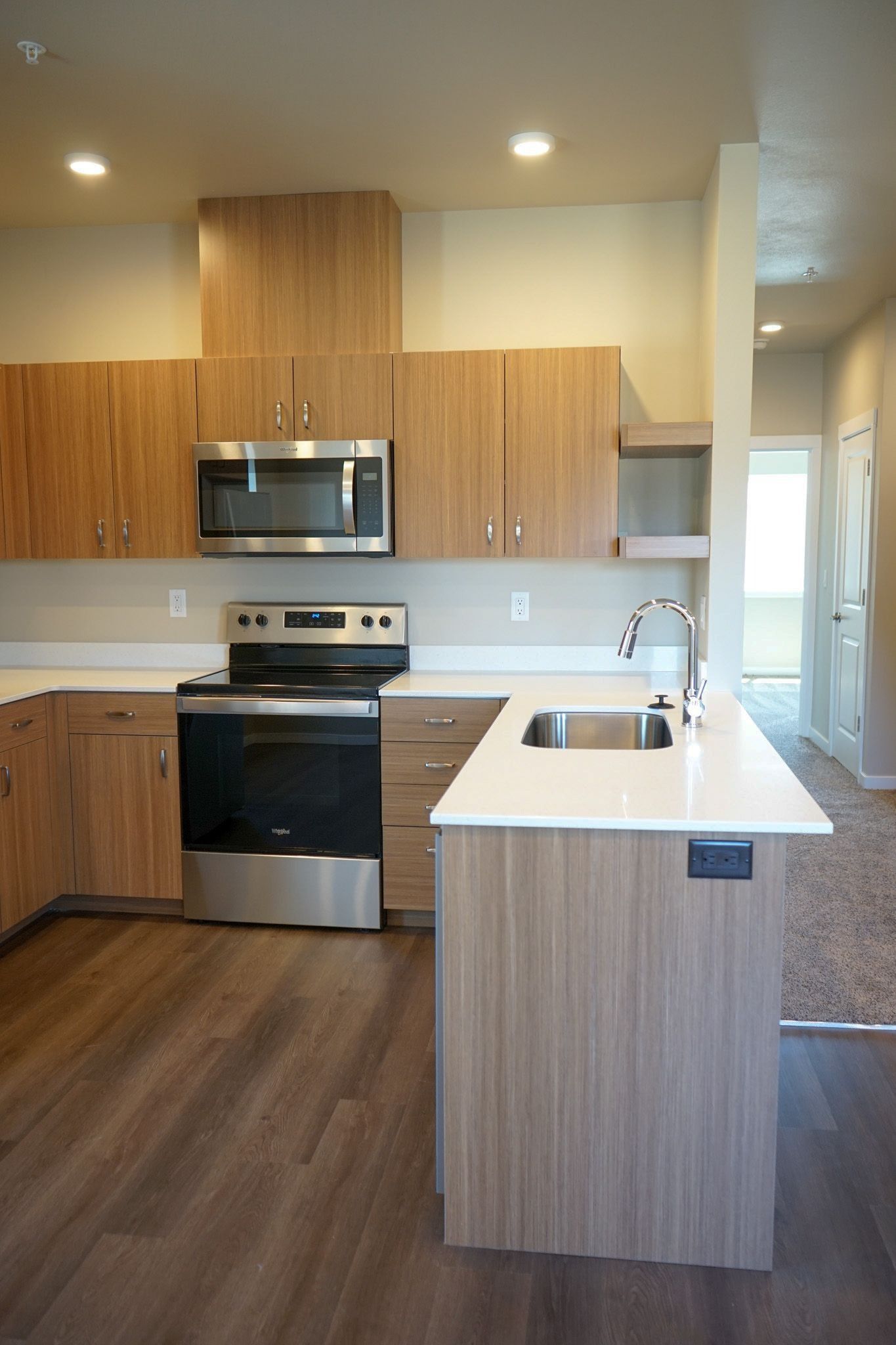 Modern kitchen with wood cabinets, white island, stainless steel appliances, and recessed lighting.