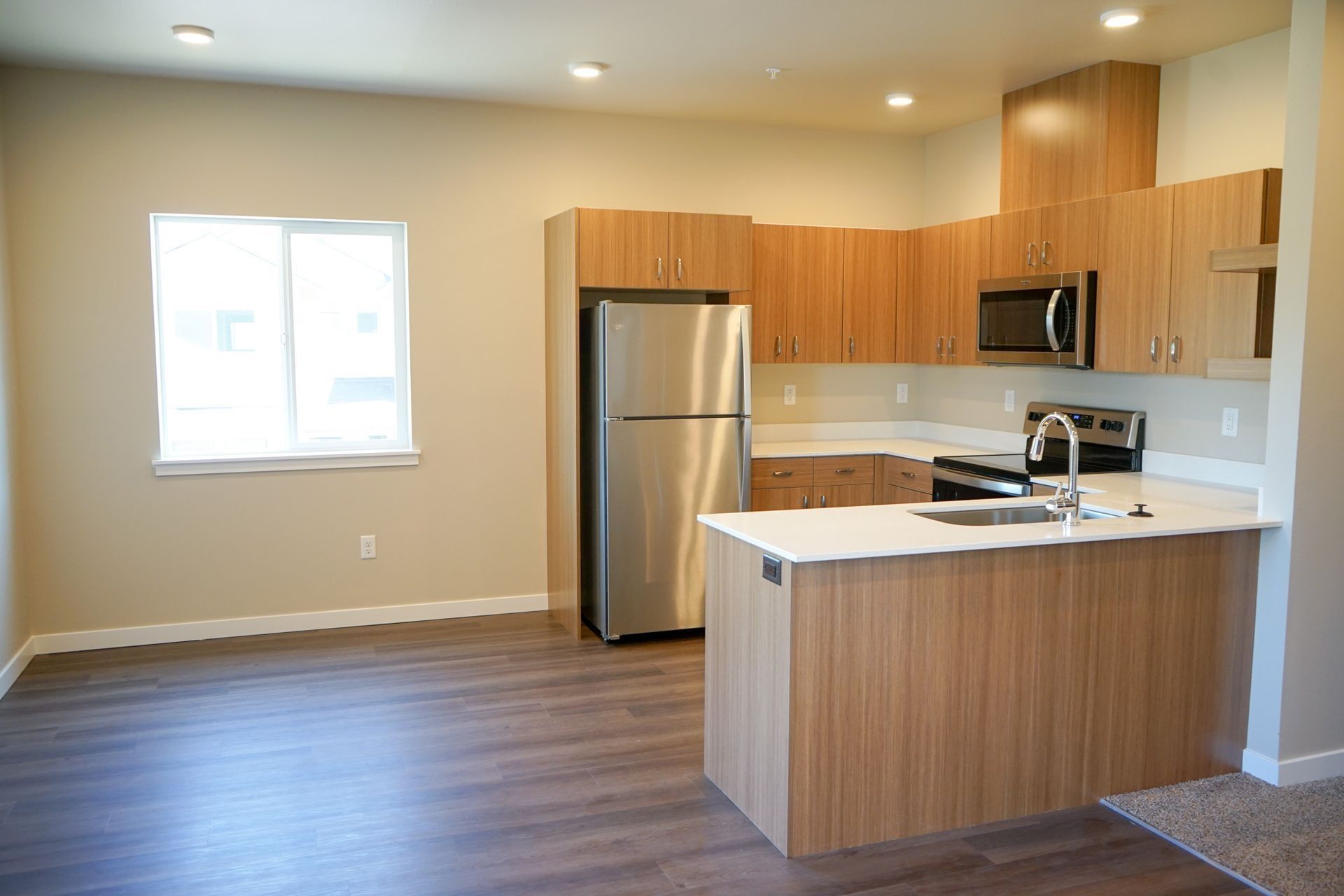 Empty modern kitchen with wood cabinets, stainless steel appliances, white countertops, and a window
