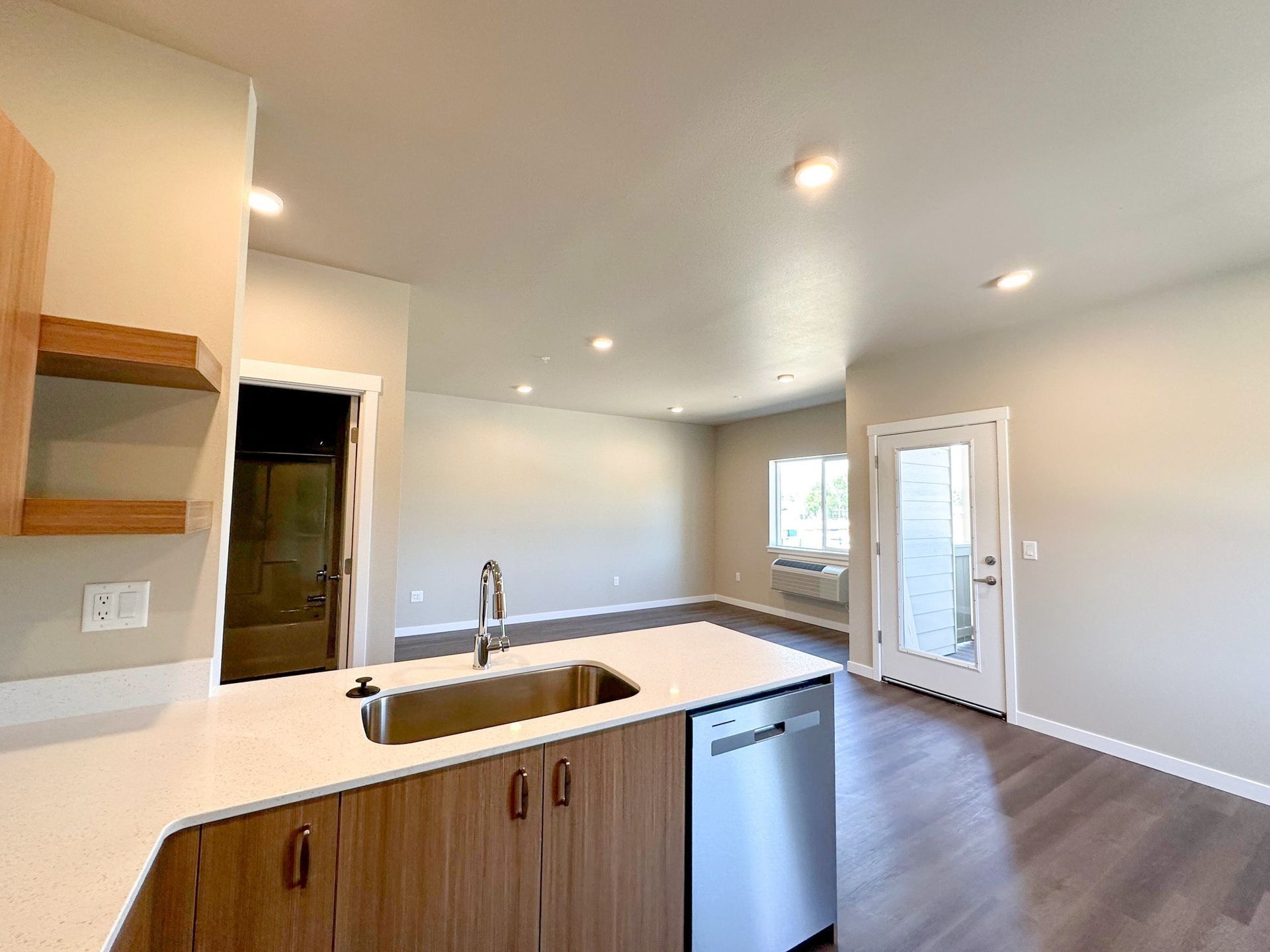 Empty modern kitchen and living area with white cabinets, island sink, and gray wood floors