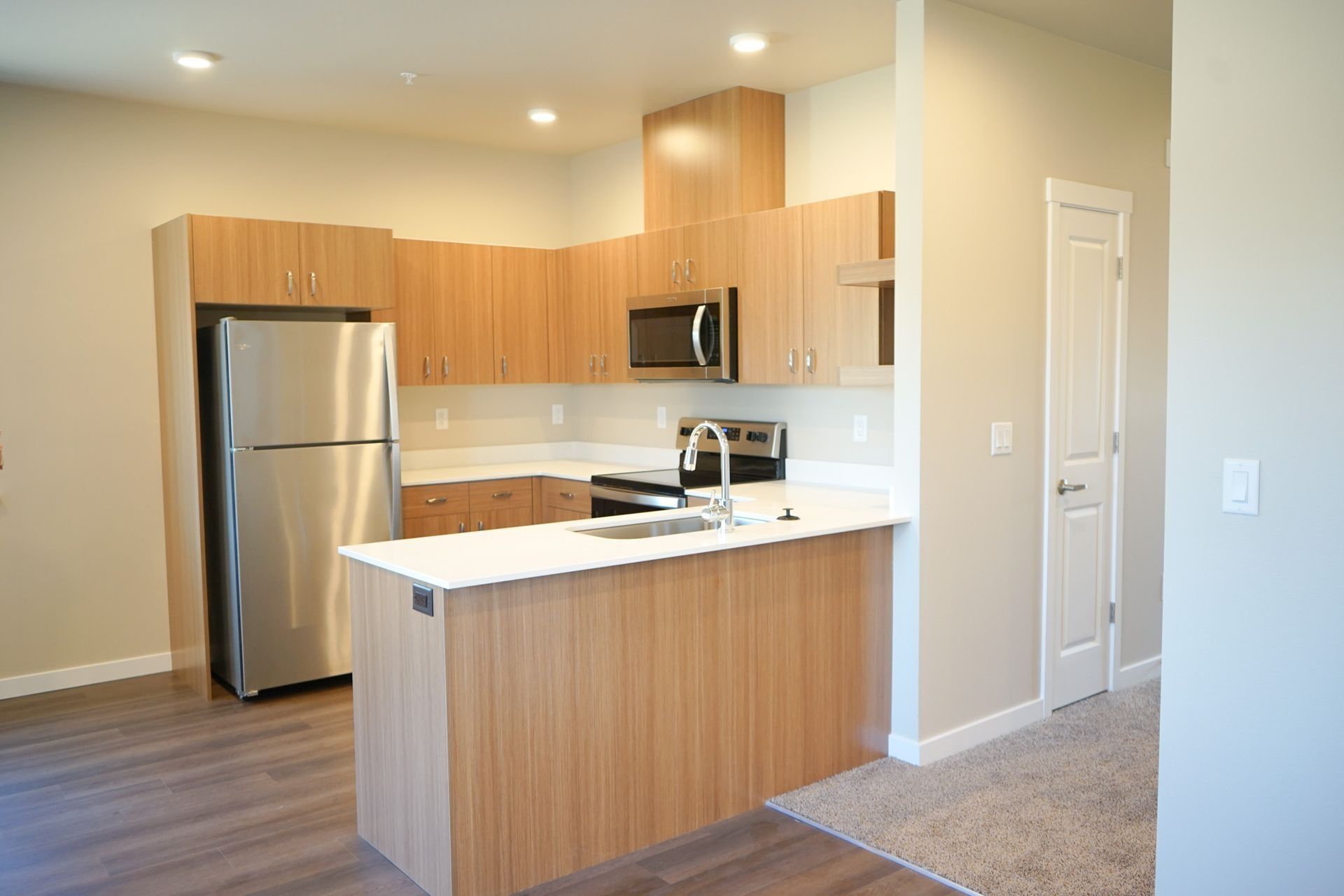 Modern kitchen with stainless steel appliances, wood cabinets, white island, and gray walls.