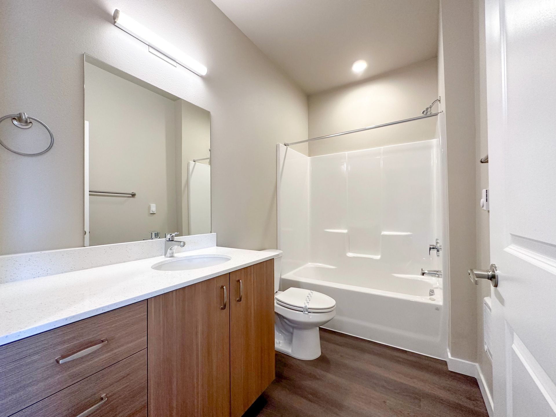 Modern bathroom with wood vanity, white sink, toilet, and bathtub/shower combo