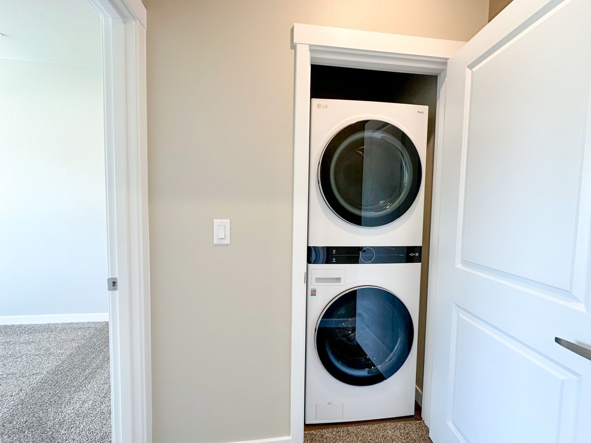 Stacked washer and dryer in a hallway closet with white doors open