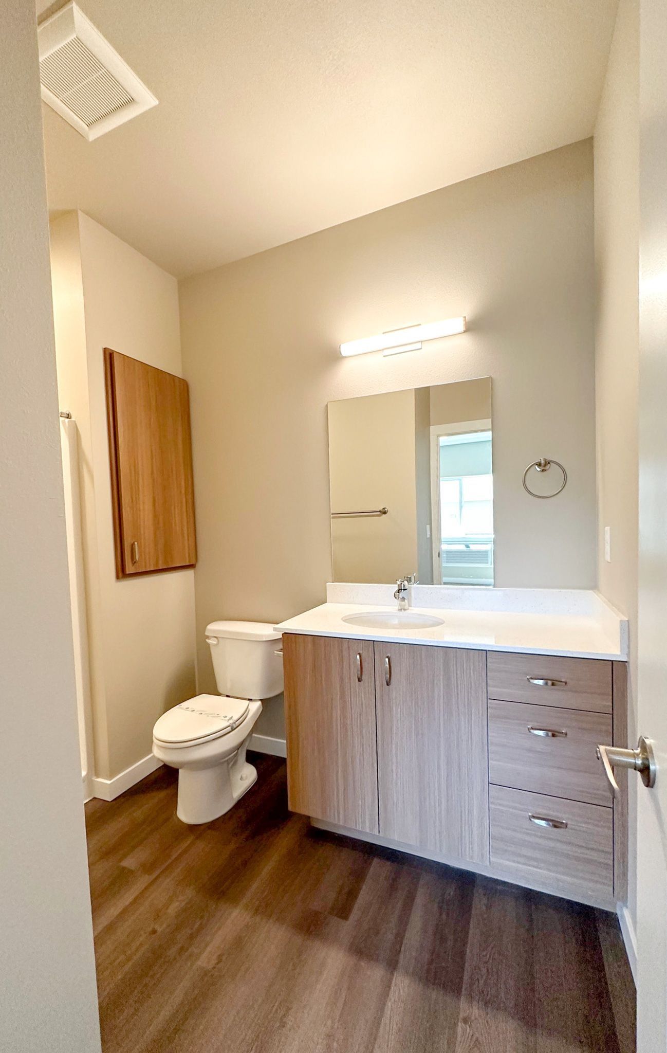 Modern bathroom with wood vanity, white sink, toilet, mirror, and wall light.