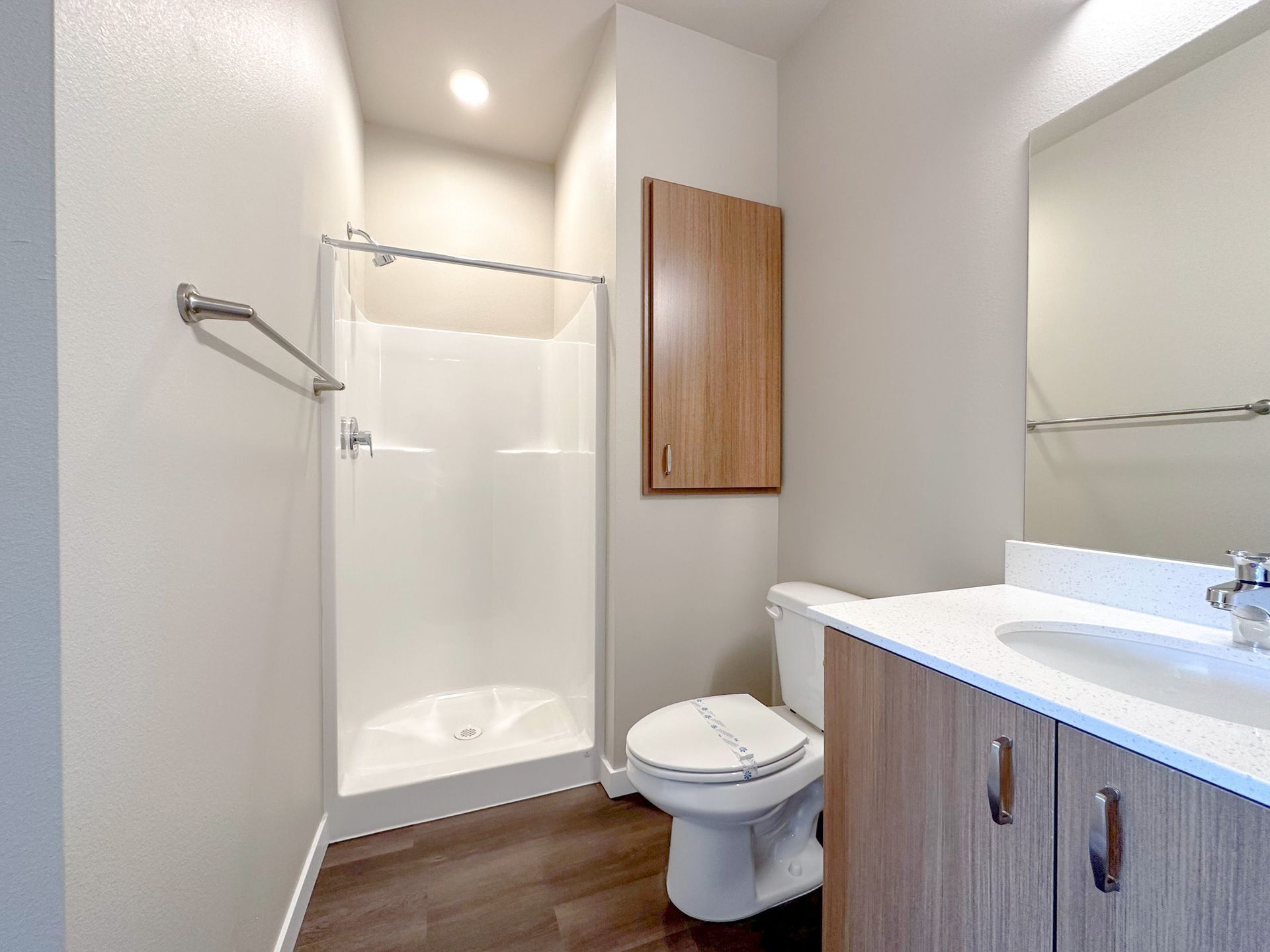Small bathroom with shower, toilet, white sink, and wood vanity cabinet.