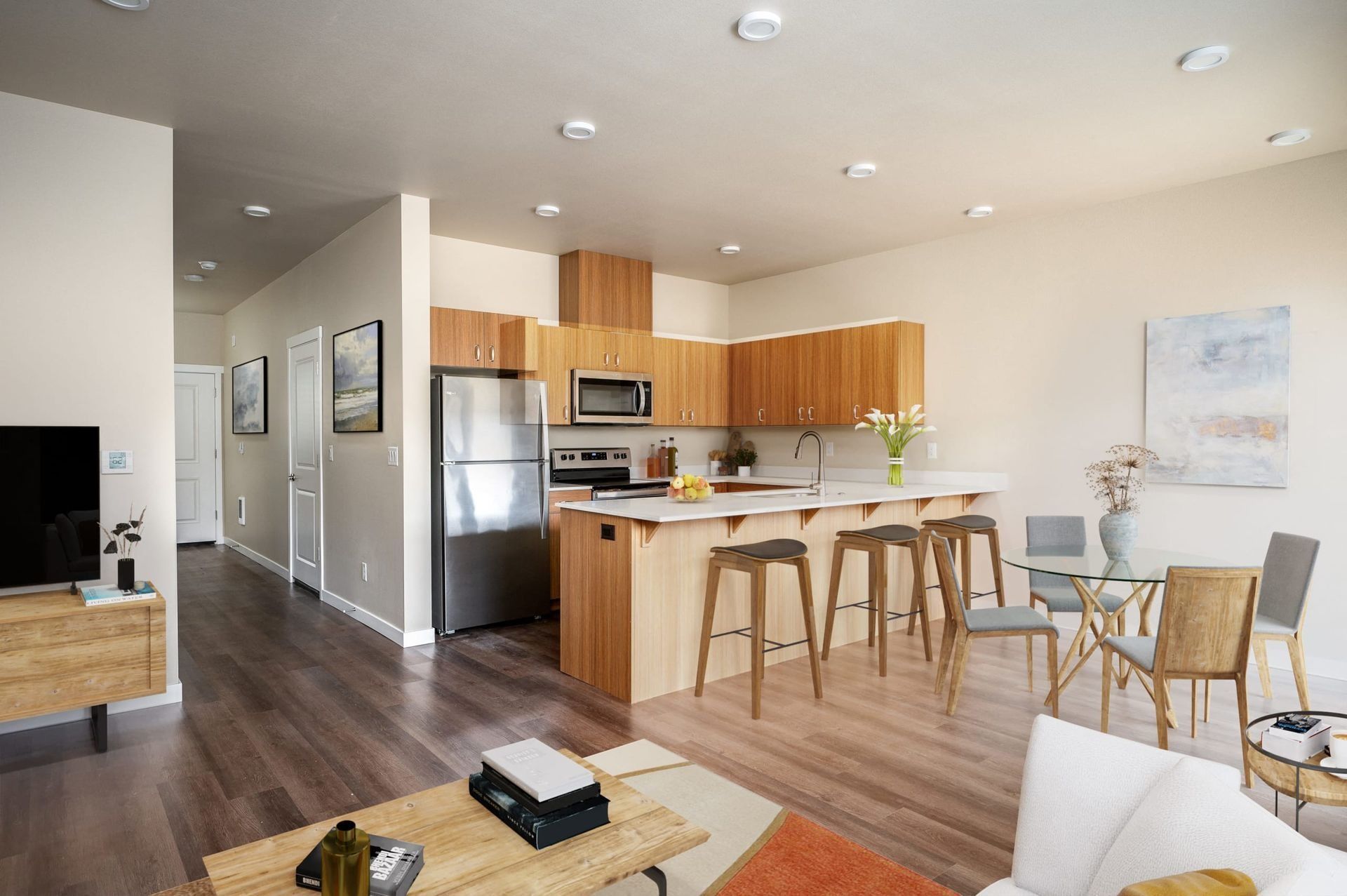 Bright modern open-plan kitchen and living room with wood floors, stainless appliances, island stools, and sofa.