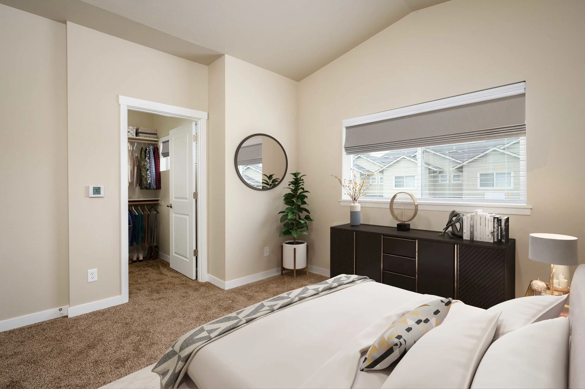 Bright bedroom with bed, dresser, round mirror, plant, and window with blinds