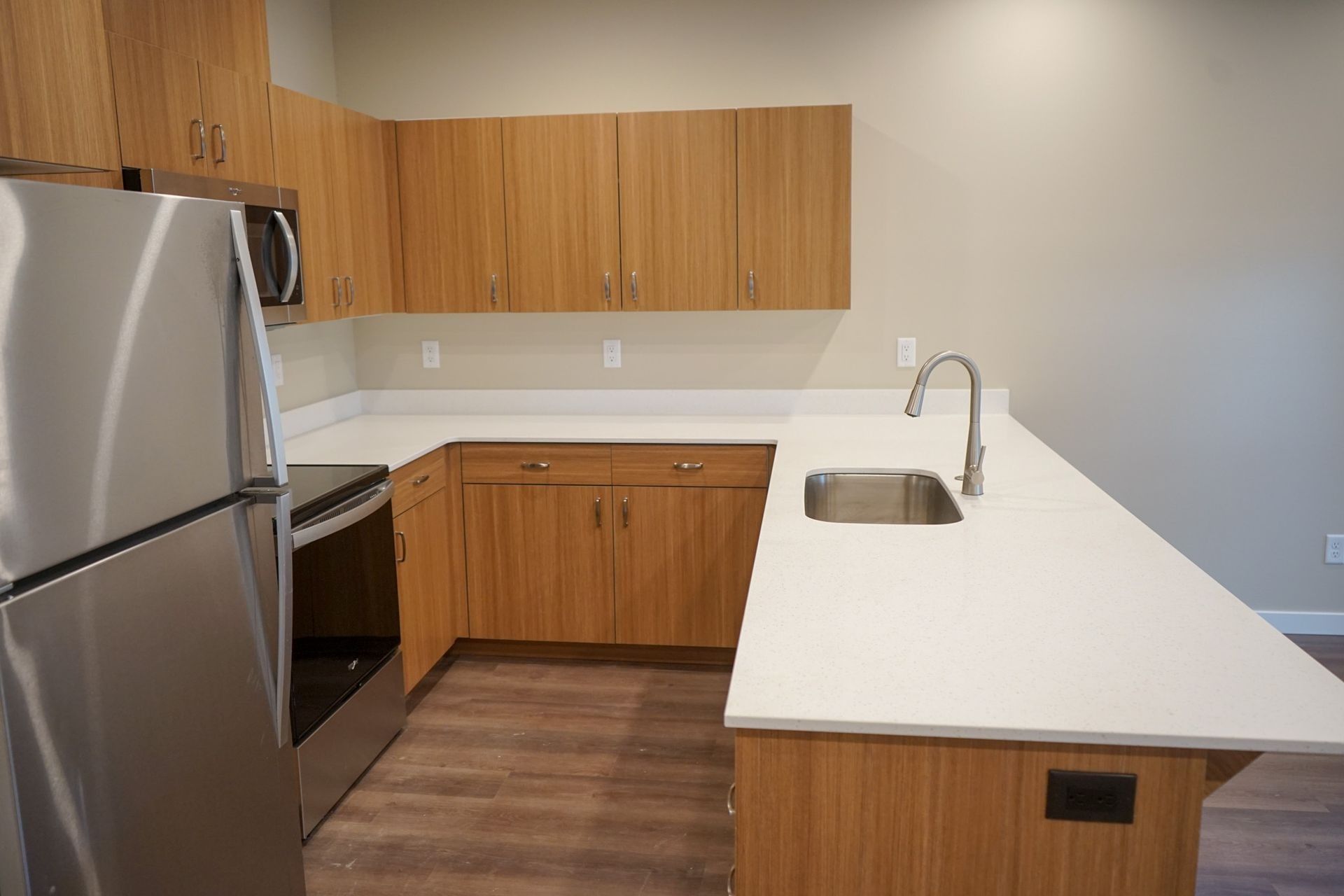 Modern kitchen with wood cabinets, stainless steel appliances, white countertops, and a sink island