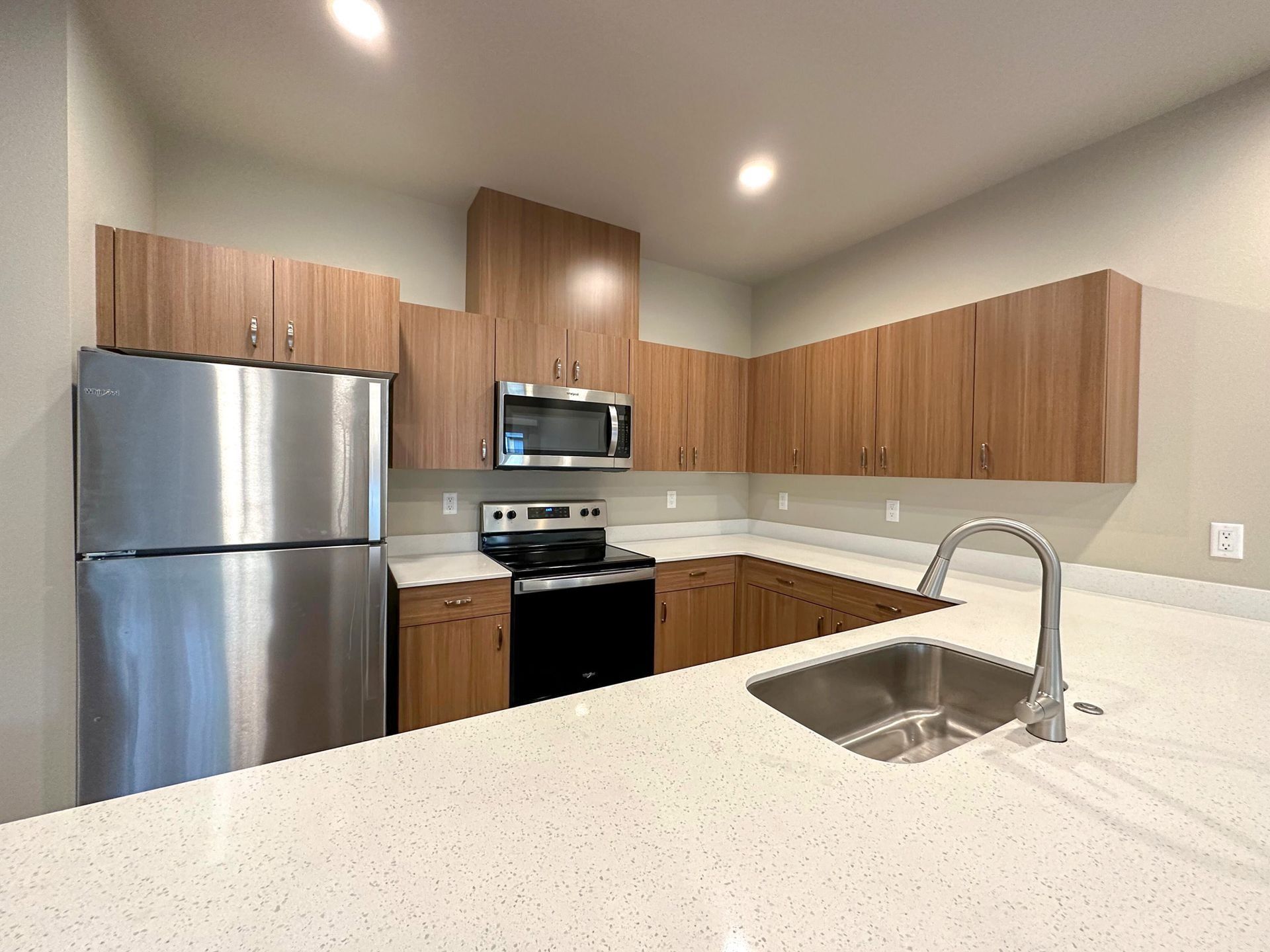Modern kitchen with stainless appliances, wood cabinets, and a white speckled countertop with sink