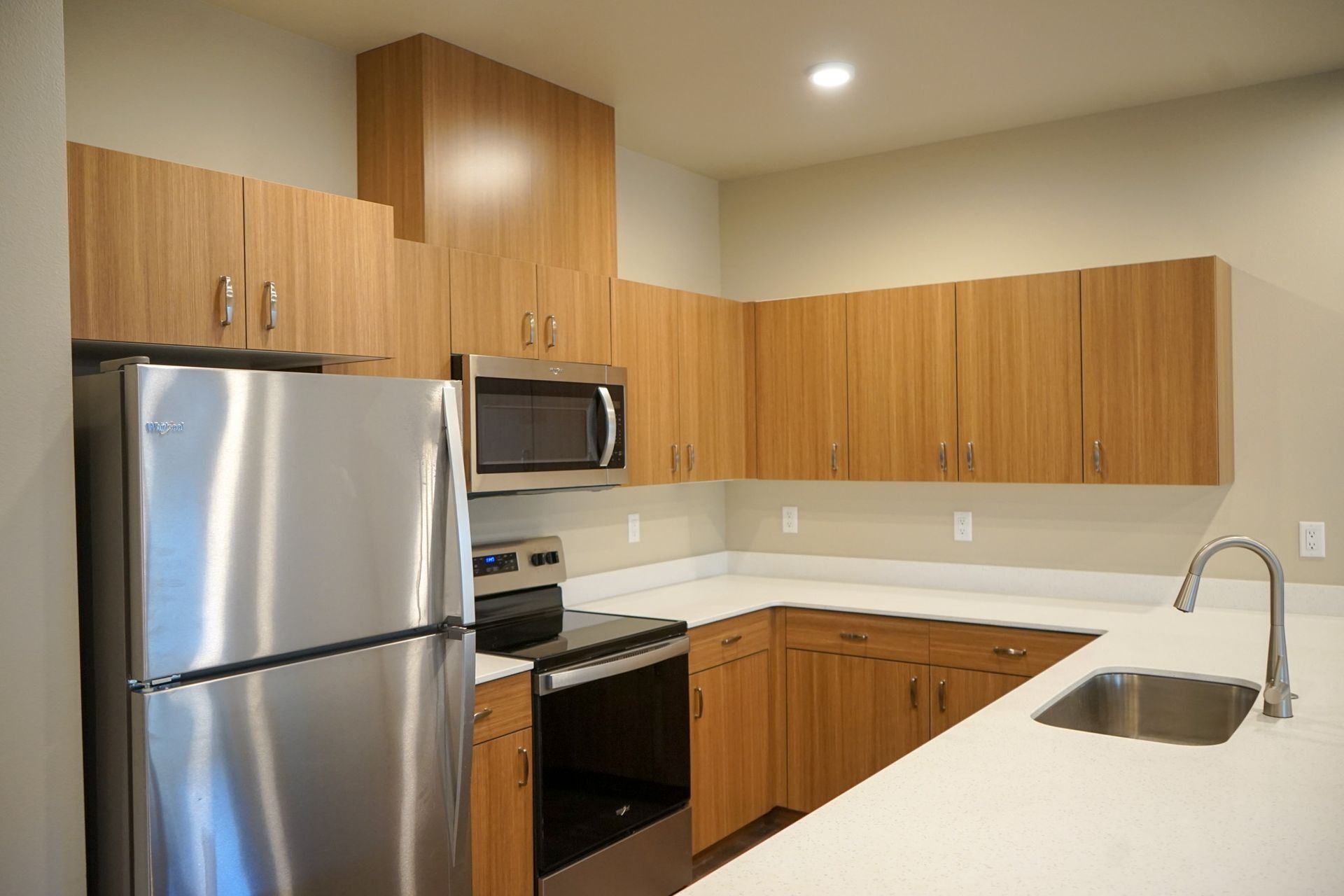 Modern kitchen with stainless steel appliances, wood cabinets, and a white countertop with sink