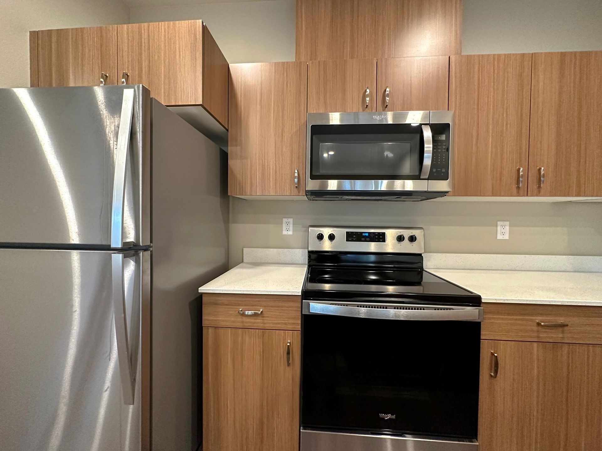 Modern kitchen with stainless steel fridge, black stove, microwave, and wood cabinets.