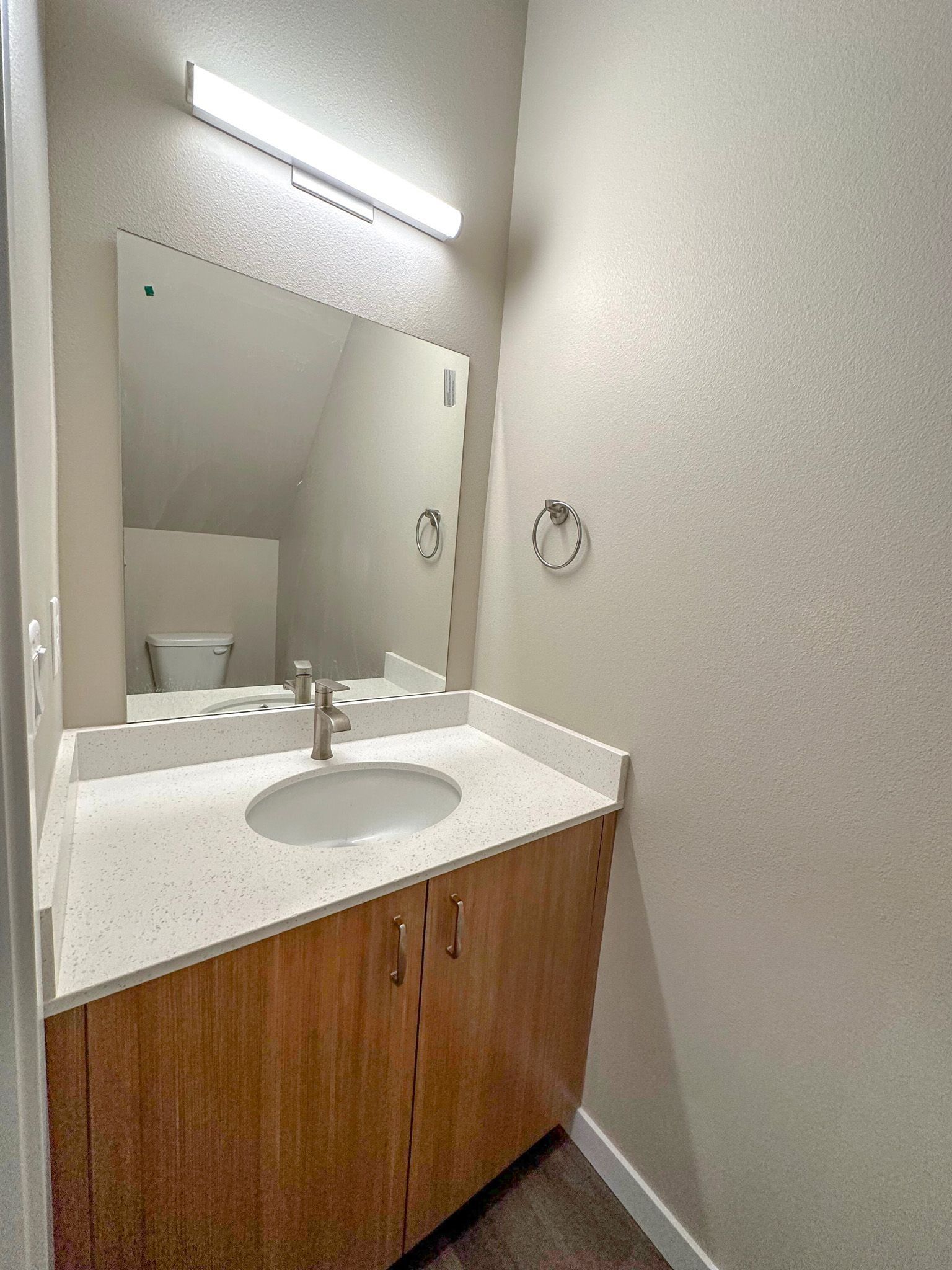 Small bathroom vanity with sink, mirror, and wall light above a wood cabinet.
