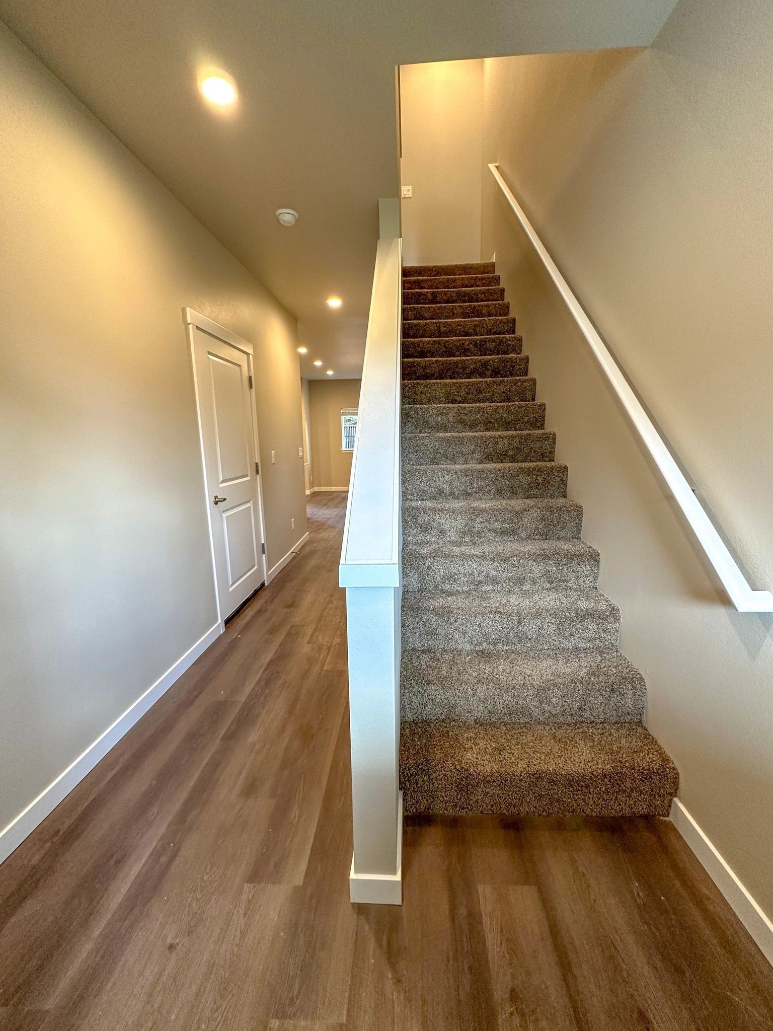 Hallway with wood floors and carpeted stairs, beige walls, and white trim leading upward