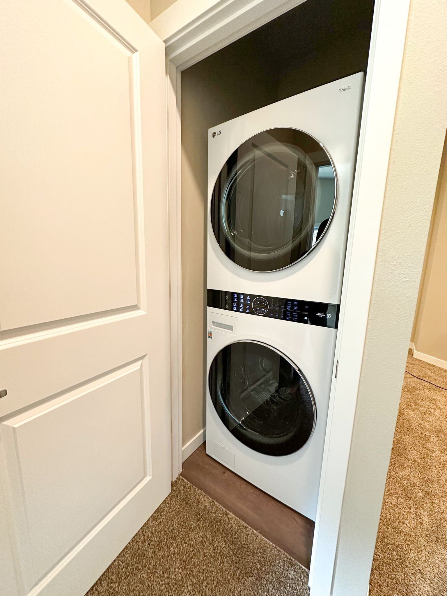 Stacked washer and dryer in a closet, with white doors partly open.