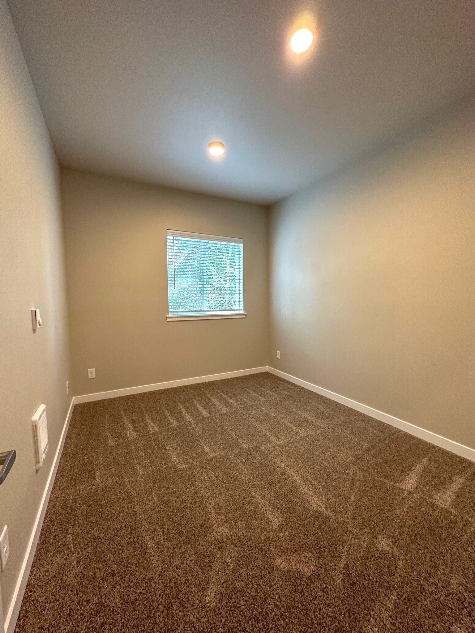 Empty beige carpeted room with single window and ceiling light