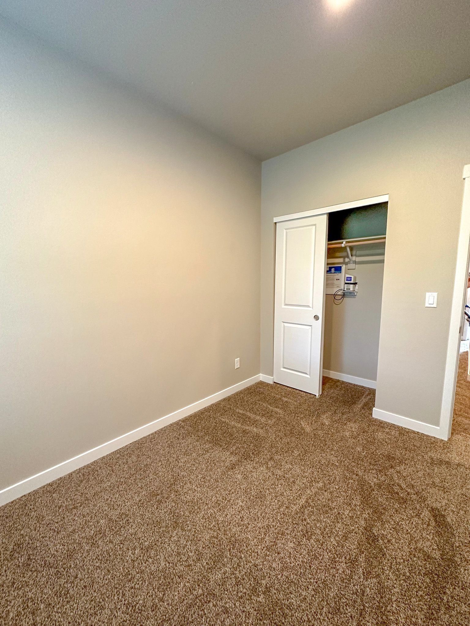 Empty beige carpeted room with white walls, a closet door, and an open doorway.