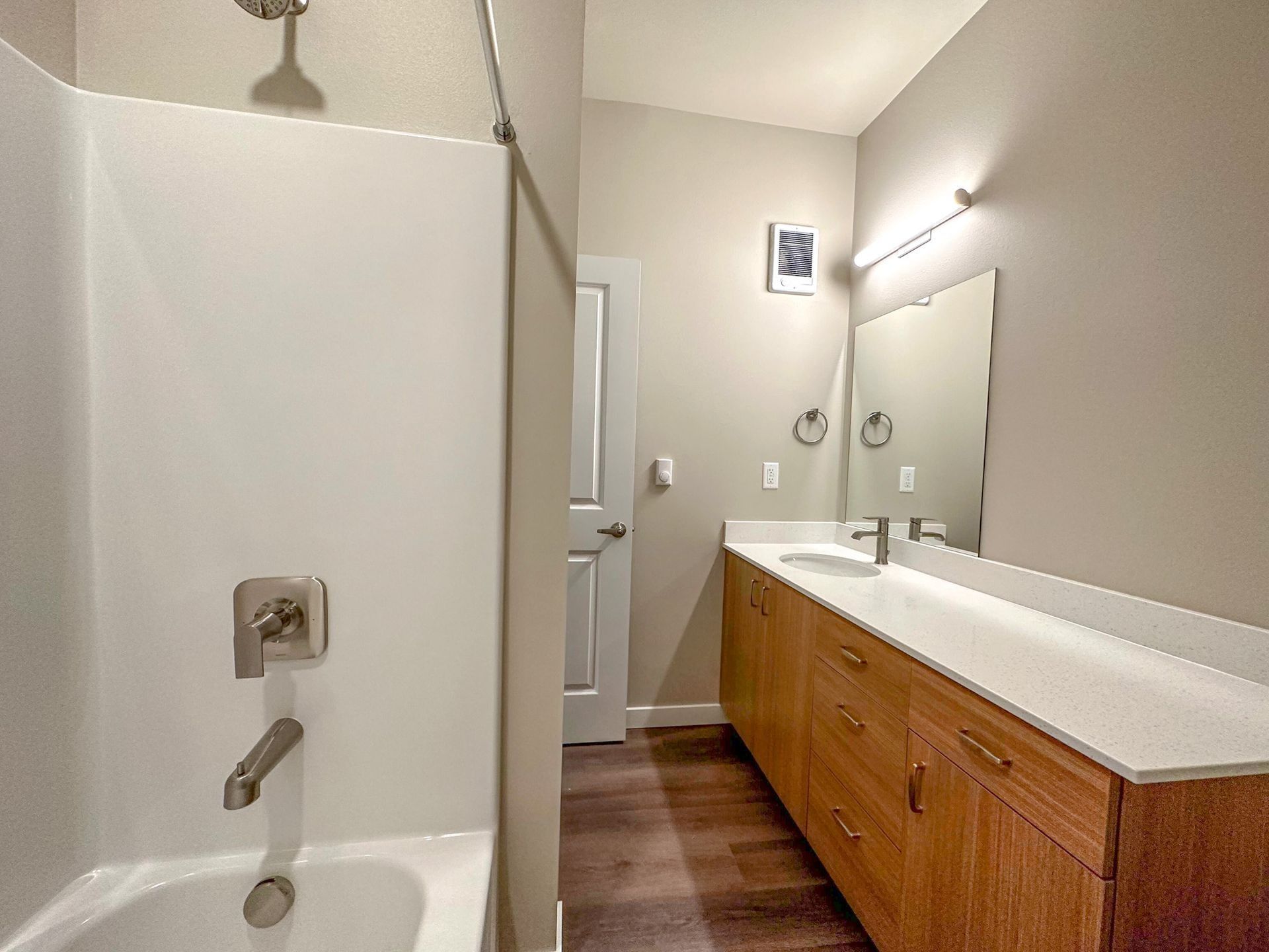 Bathroom with shower on left, white sink vanity on right, mirror, and wood floor.
