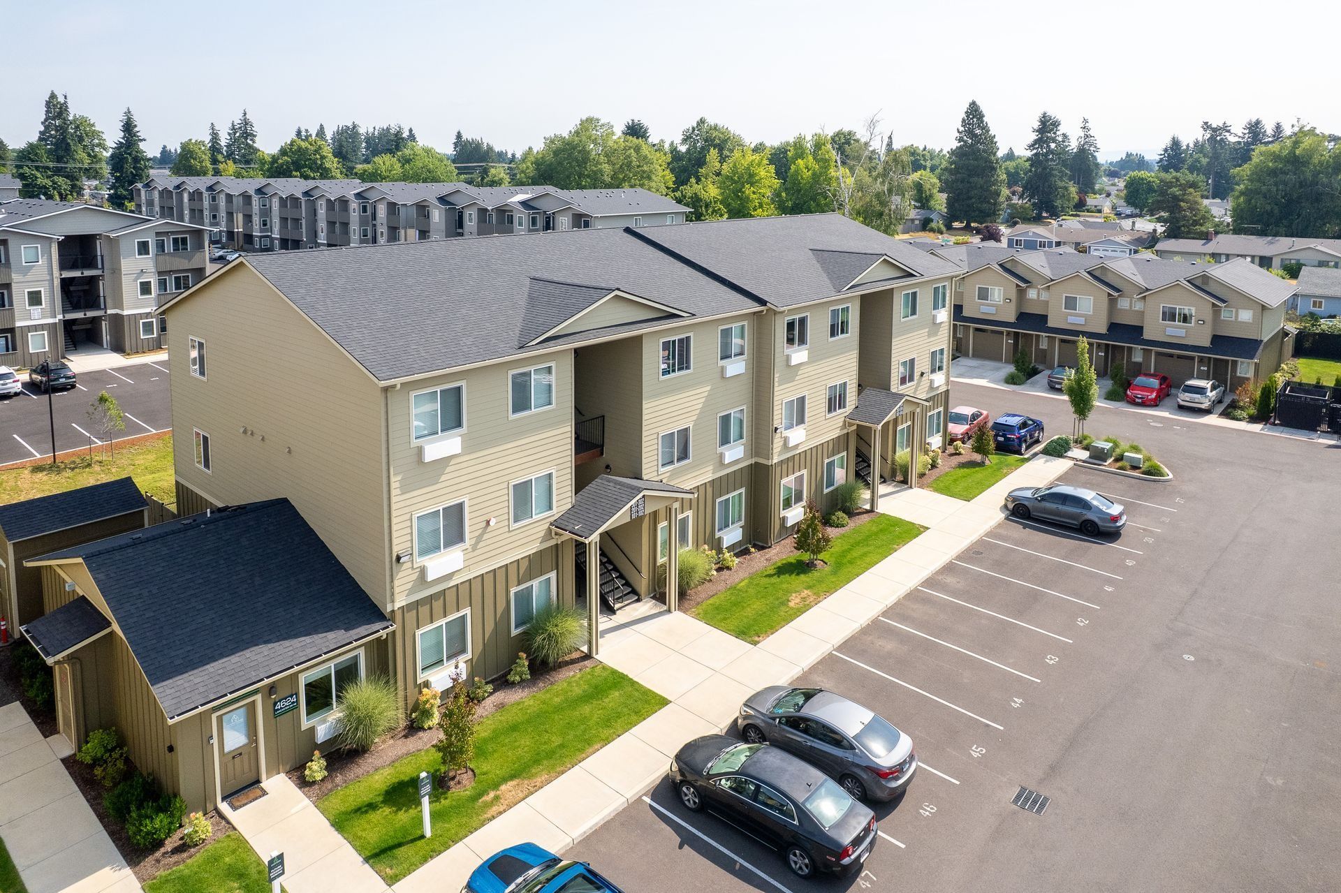 Aerial view of tan apartment buildings with parked cars in a residential complex