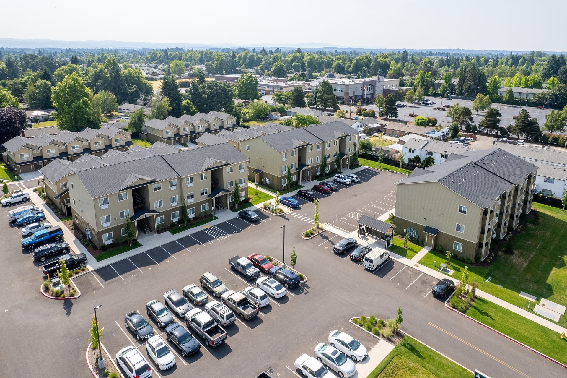 Aerial view of apartment complex with parking lots, cars, and green trees on a sunny day
