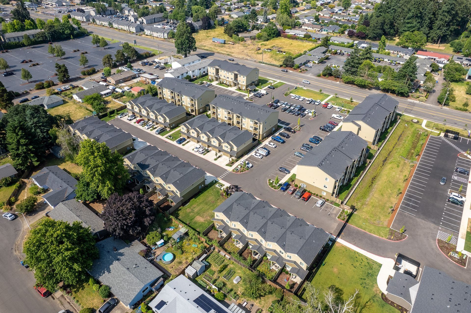 Aerial view of a suburban apartment complex with parking lots, roads, and surrounding trees