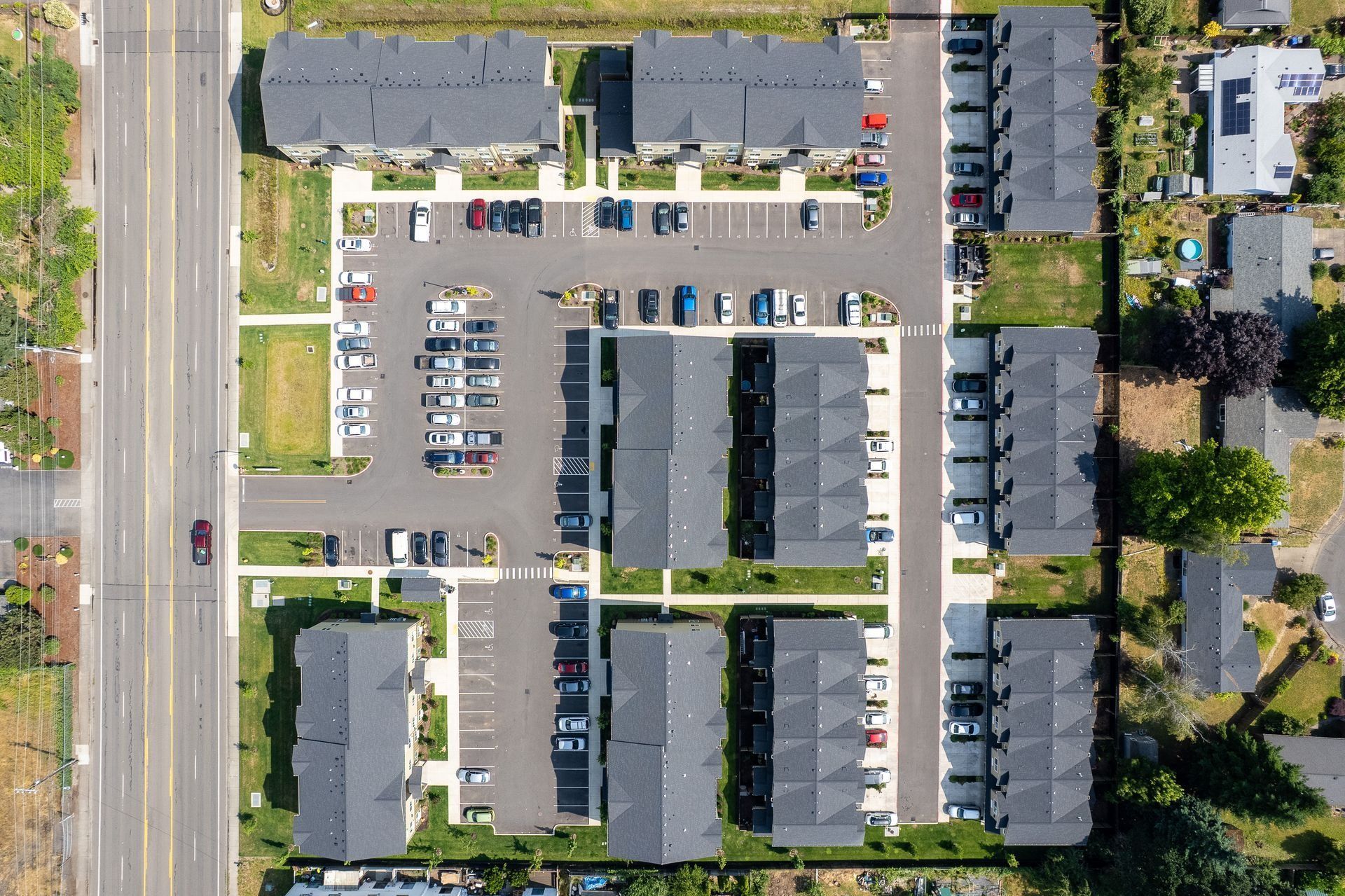 Aerial view of a parking lot and apartment complex with parked cars and surrounding trees.