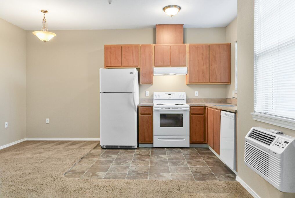 Small kitchen with white appliances, wood cabinets, and beige tile floor in a bright apartment.