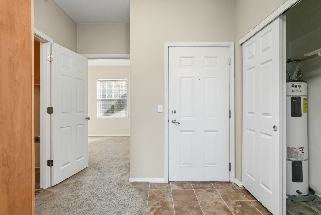Bright hallway with white doors, beige walls, carpeted room, and a tiled entry area.