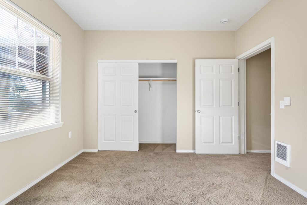 Empty beige bedroom with carpet, closet, window, and open door to the right